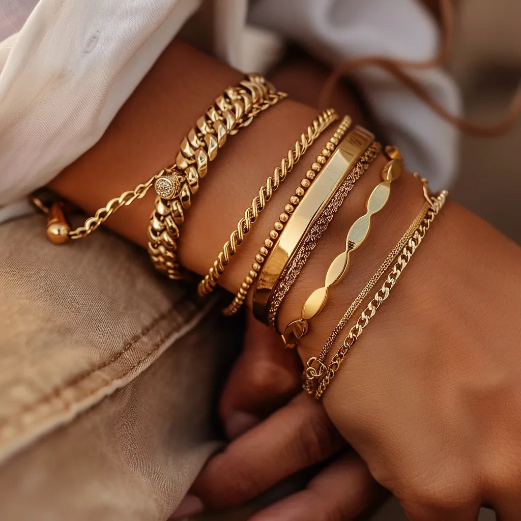A close-up image of a woman's wrist adorned with a variety of gold bracelets. The collection features diverse designs including chunky chains, delicate filigree, sleek bangles, and bracelets with embedded gemstones, all showcasing a rich golden hue.