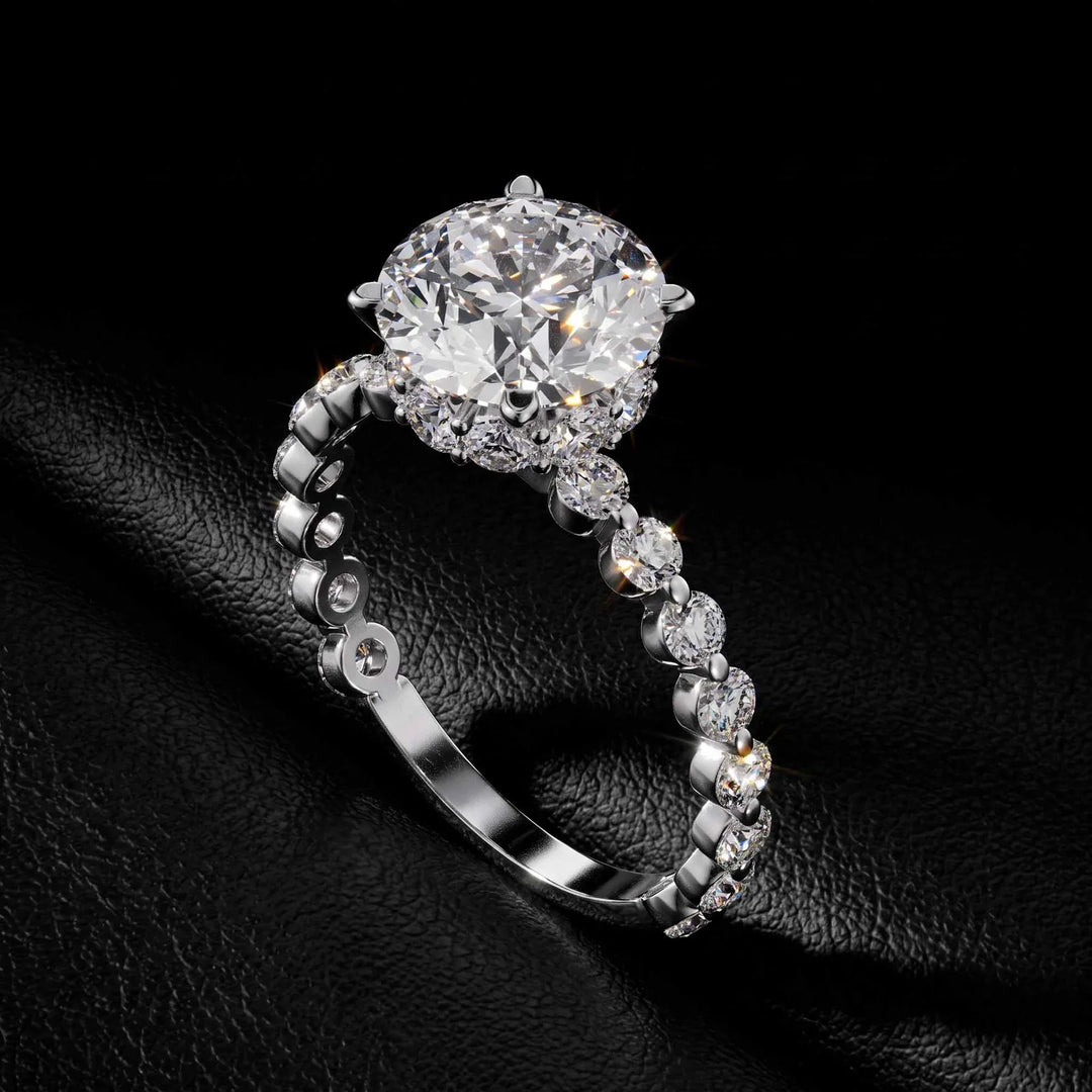 Round diamond hidden-halo engagement ring with a shared-prong band on a black leather surface.