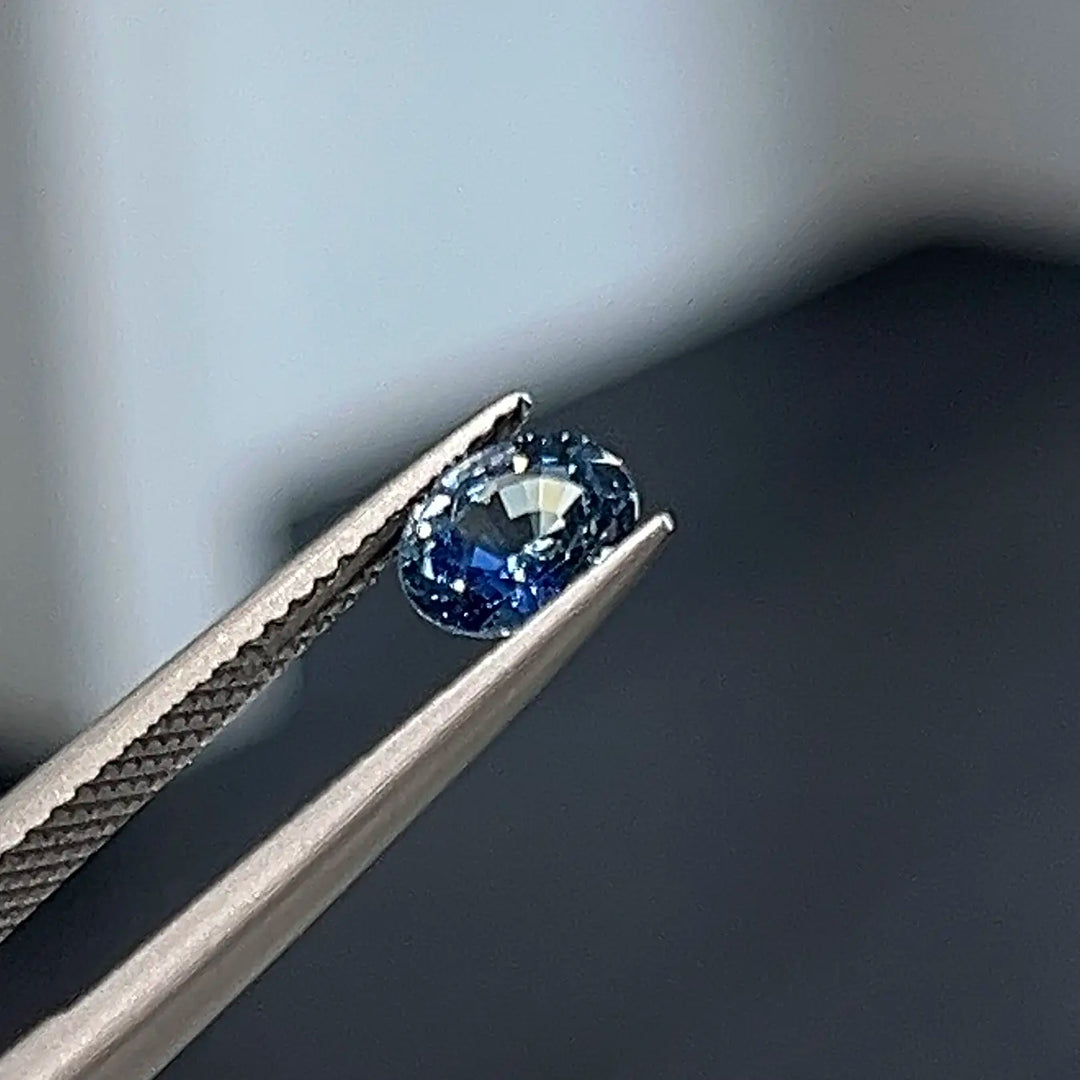 Loose oval sapphire held by tweezers for custom jewellery design