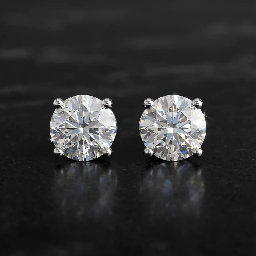 Round lab-grown diamond four-prong basket stud earrings displayed on black surface.