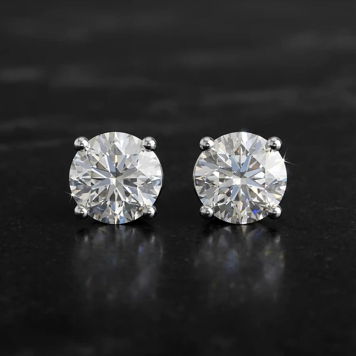 Round lab-grown diamond four-prong basket stud earrings displayed on black surface.