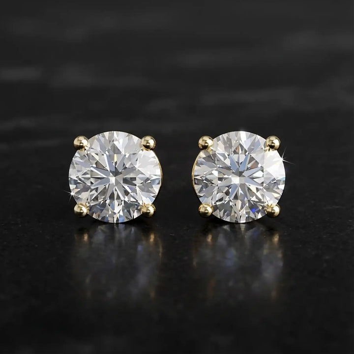 Round lab-grown diamond four-prong basket stud earrings displayed on black surface.