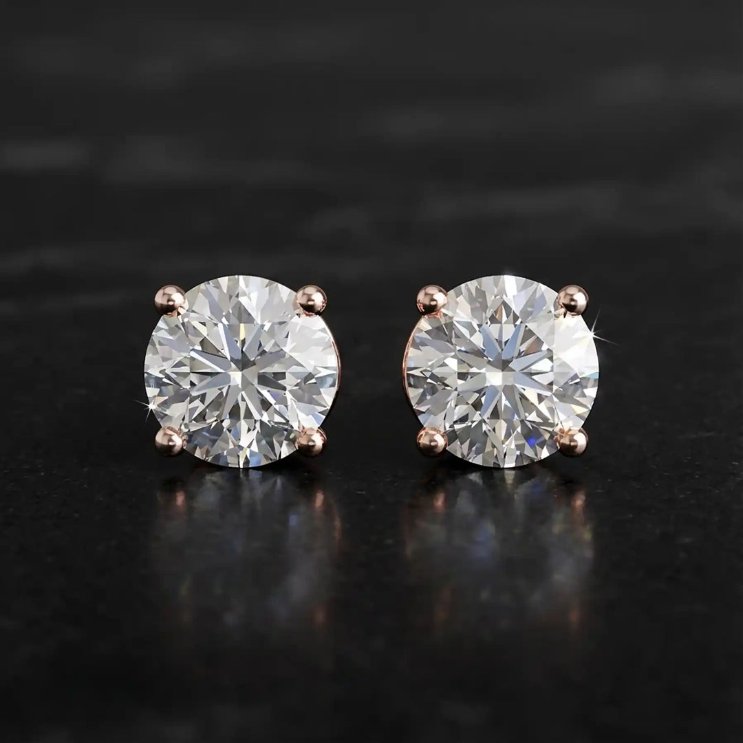 Round lab-grown diamond four-prong basket stud earrings displayed on black surface.