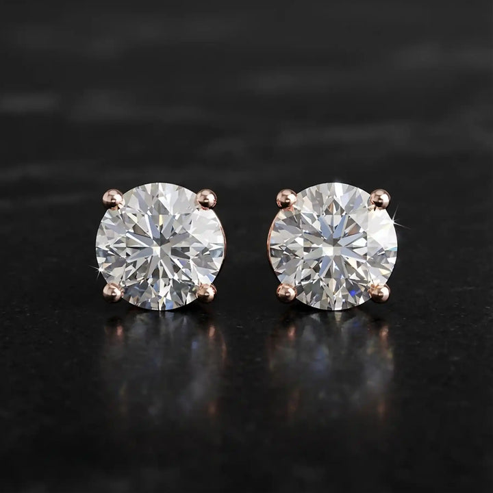 Round lab-grown diamond four-prong basket stud earrings displayed on black surface.