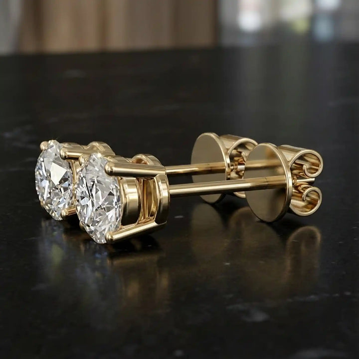 Round lab-grown diamond four-prong basket stud earrings displayed on black surface.