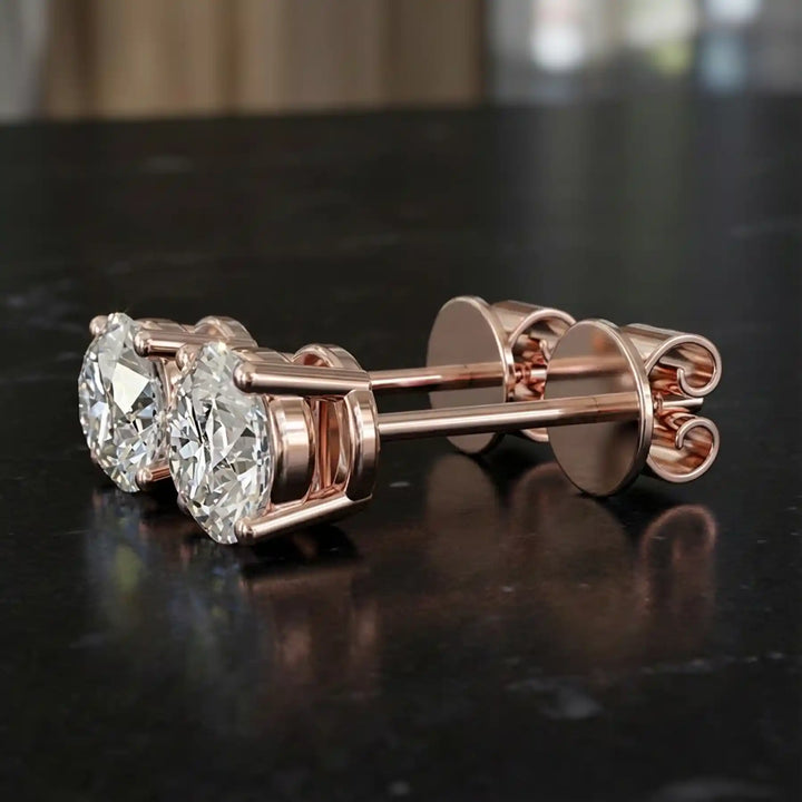 Round lab-grown diamond four-prong basket stud earrings displayed on black surface.
