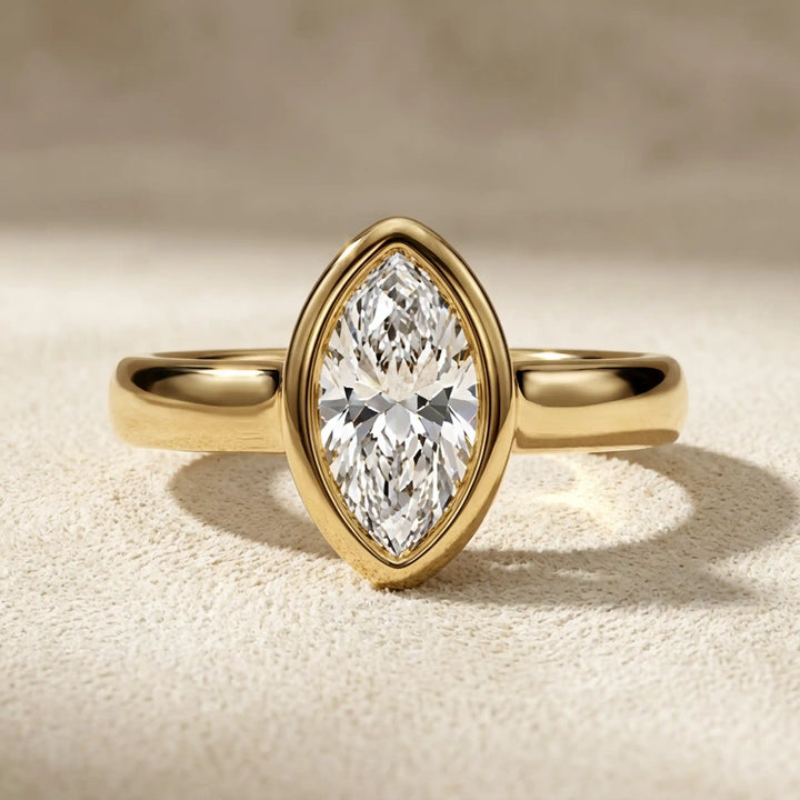 Marquise lab-grown diamond bezel engagement ring displayed on a soft surface.
