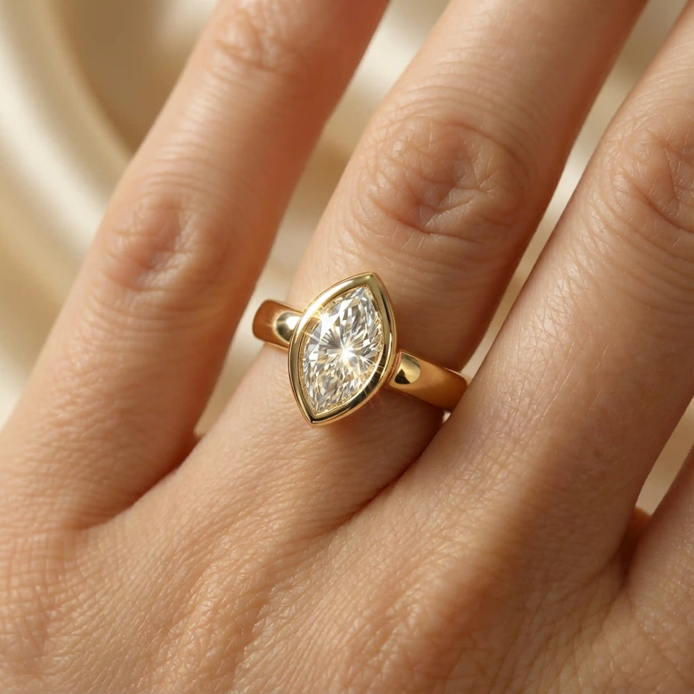 Marquise lab-grown diamond bezel engagement ring displayed on a soft surface.
