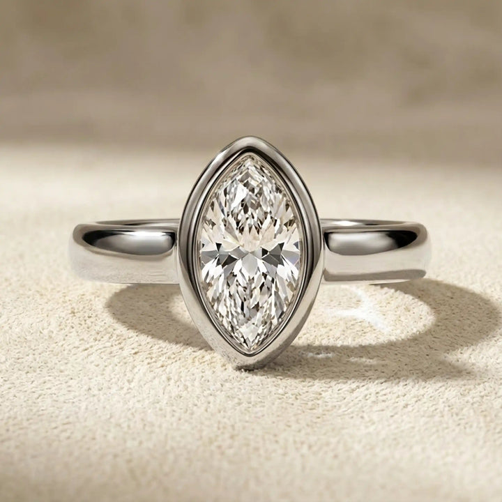 Marquise lab-grown diamond bezel engagement ring displayed on a soft surface.
