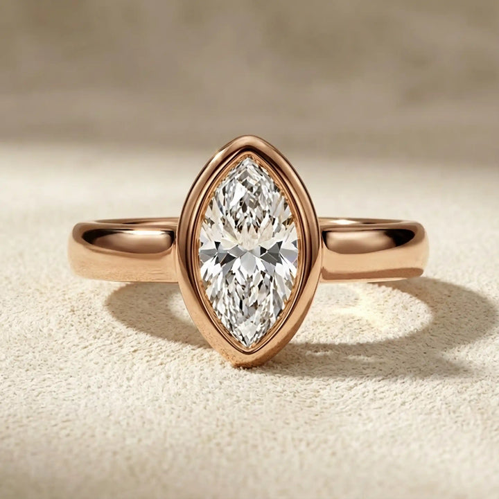 Marquise lab-grown diamond bezel engagement ring displayed on a soft surface.
