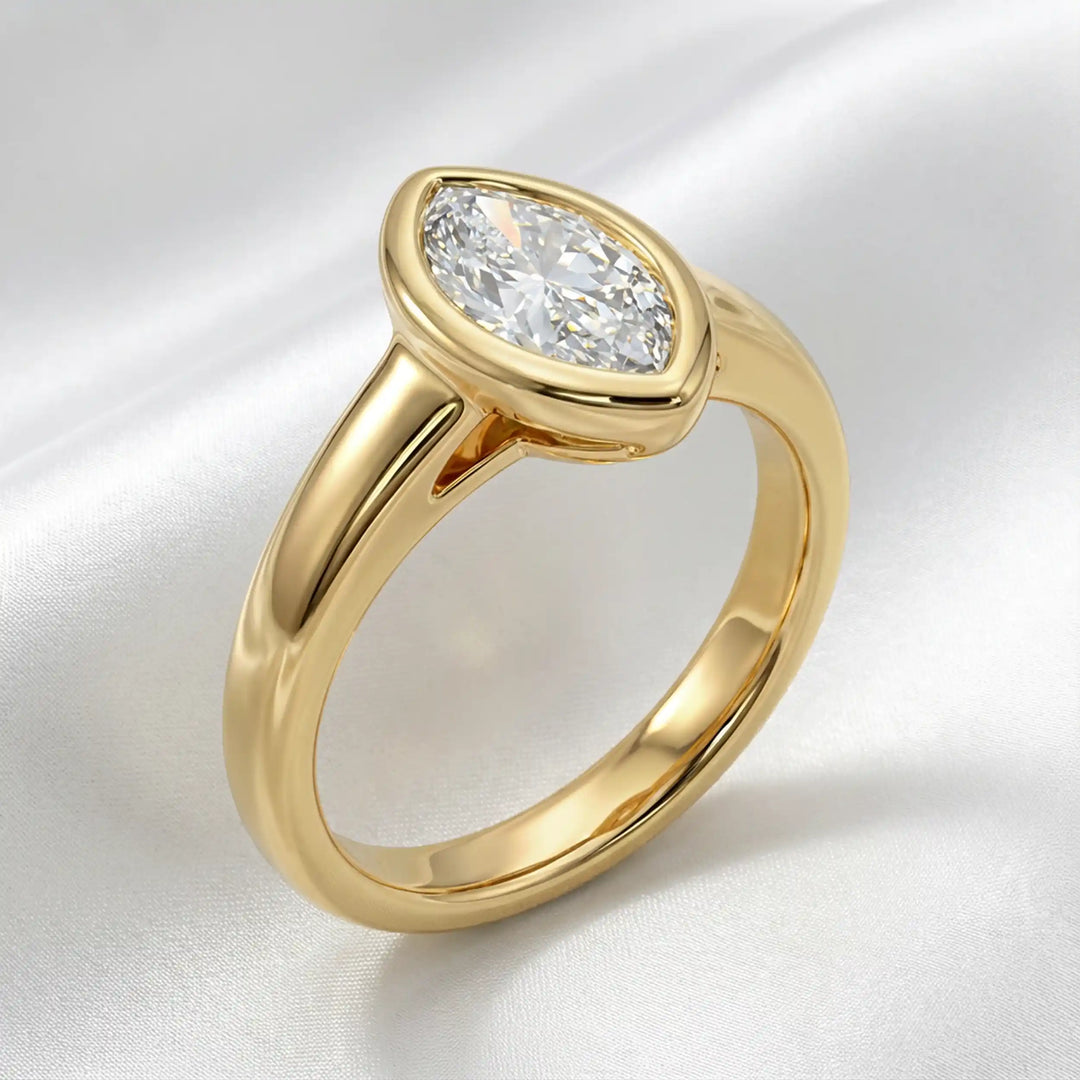 Marquise lab-grown diamond bezel engagement ring displayed on a soft surface.
