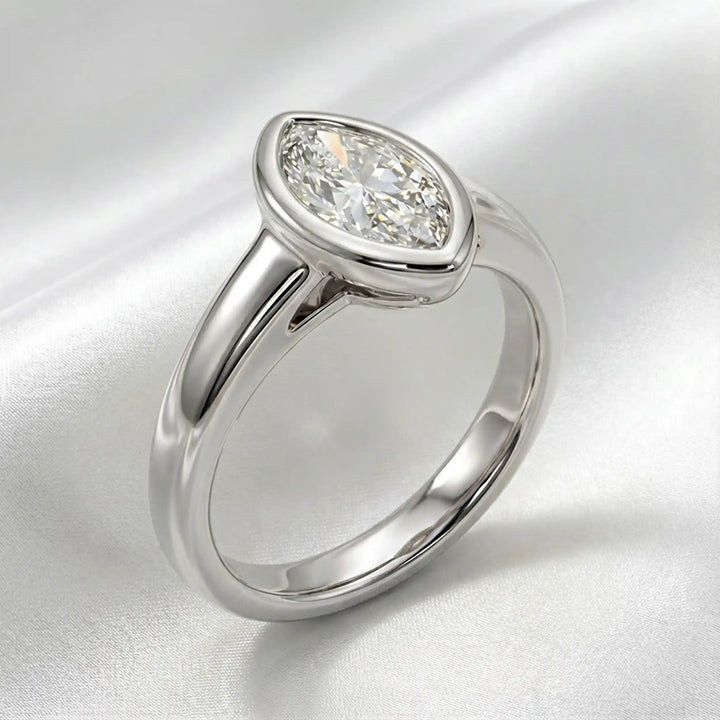 Marquise lab-grown diamond bezel engagement ring displayed on a soft surface.
