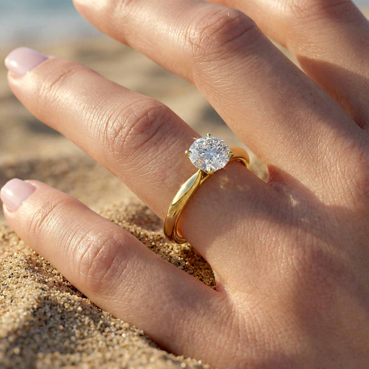 Round diamond cathedral solitaire engagement ring shown on reflective surface.
