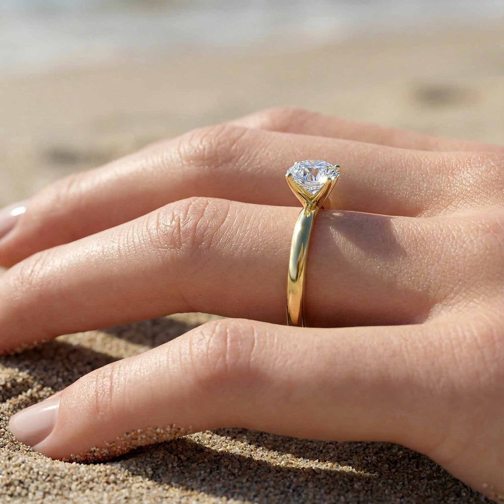 Round diamond cathedral solitaire engagement ring shown on reflective surface.