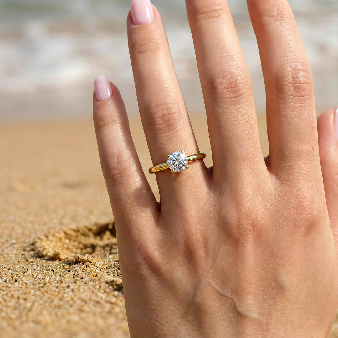 Round diamond cathedral solitaire engagement ring shown on reflective surface.
