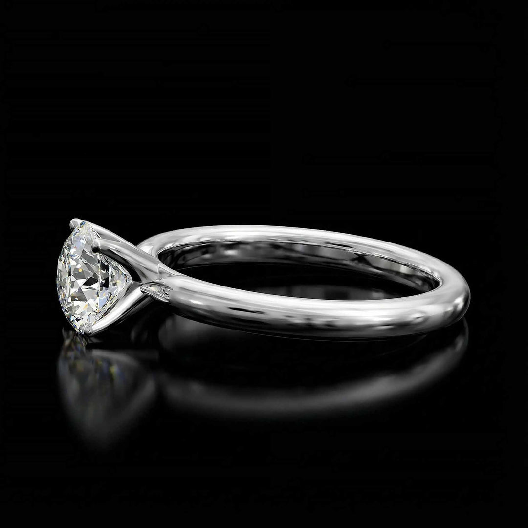 Round diamond cathedral solitaire engagement ring shown on reflective surface.
