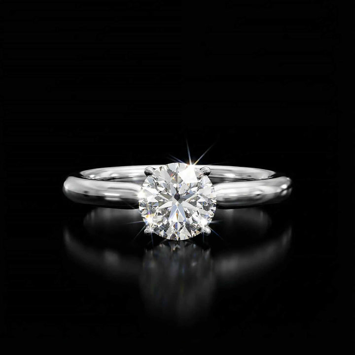 Round diamond cathedral solitaire engagement ring shown on reflective surface.
