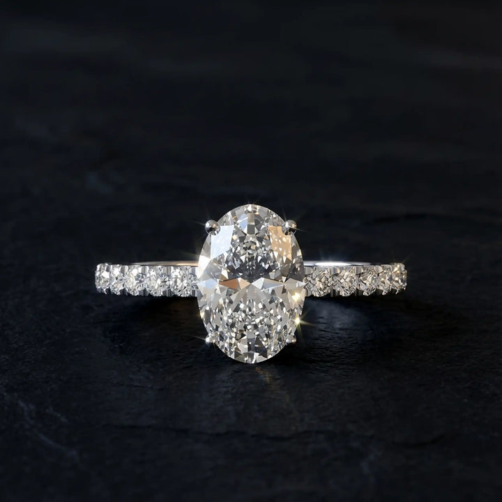 Oval lab diamond pavé engagement ring displayed on dark stone background.