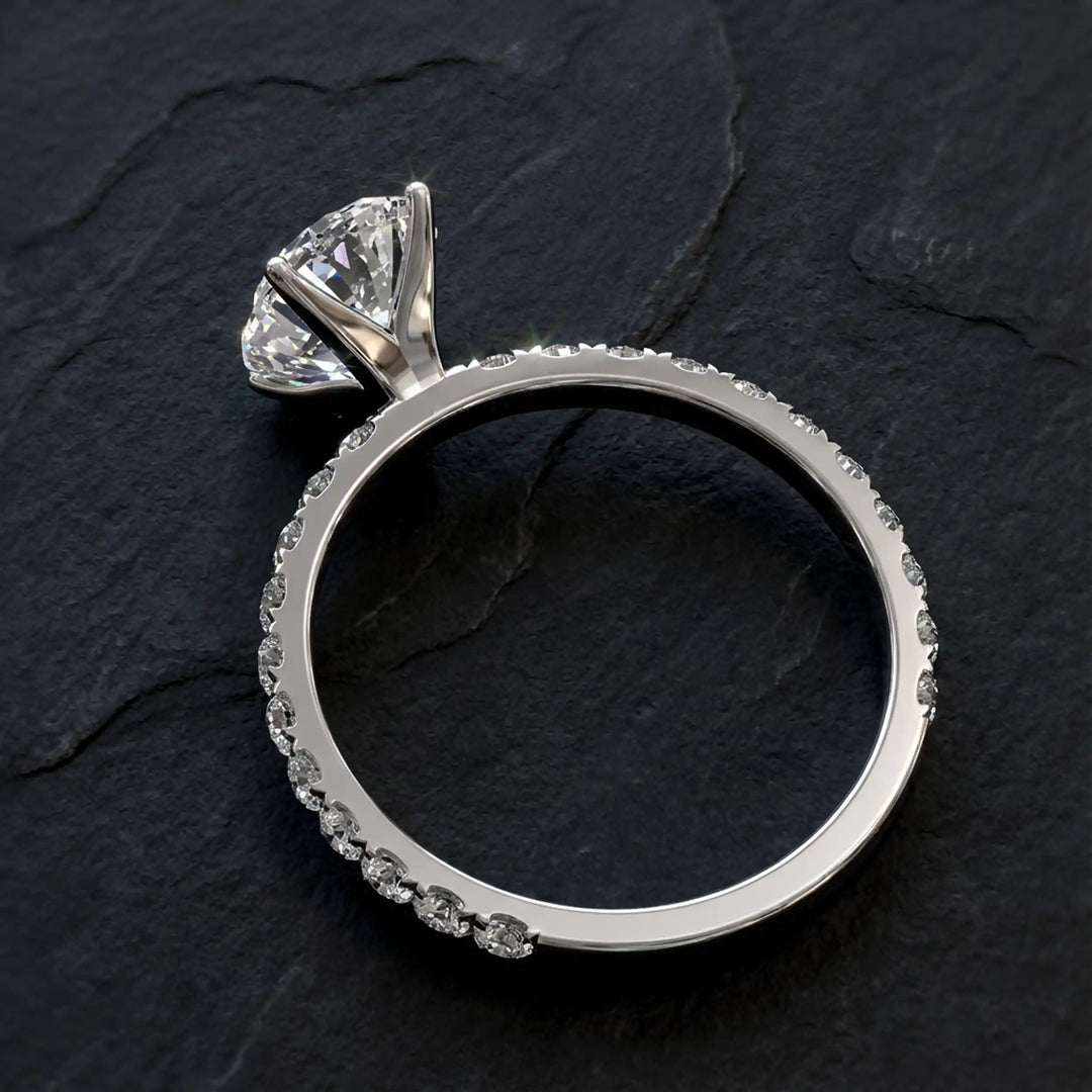 Oval lab diamond pavé engagement ring displayed on dark stone background.