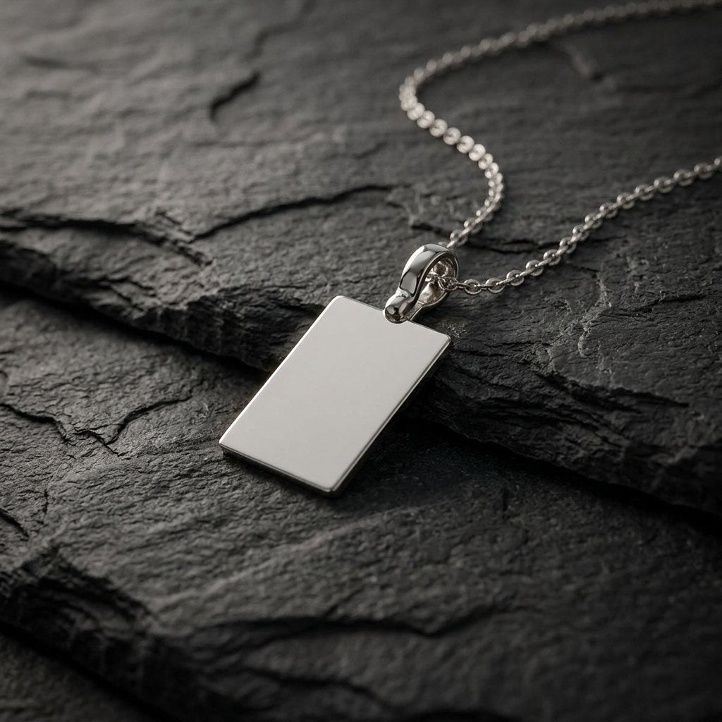 White gold plain rectangular tag pendant, 19 x 13 mm, 0.5 mm thick, on a white gold chain resting on dark slate stone