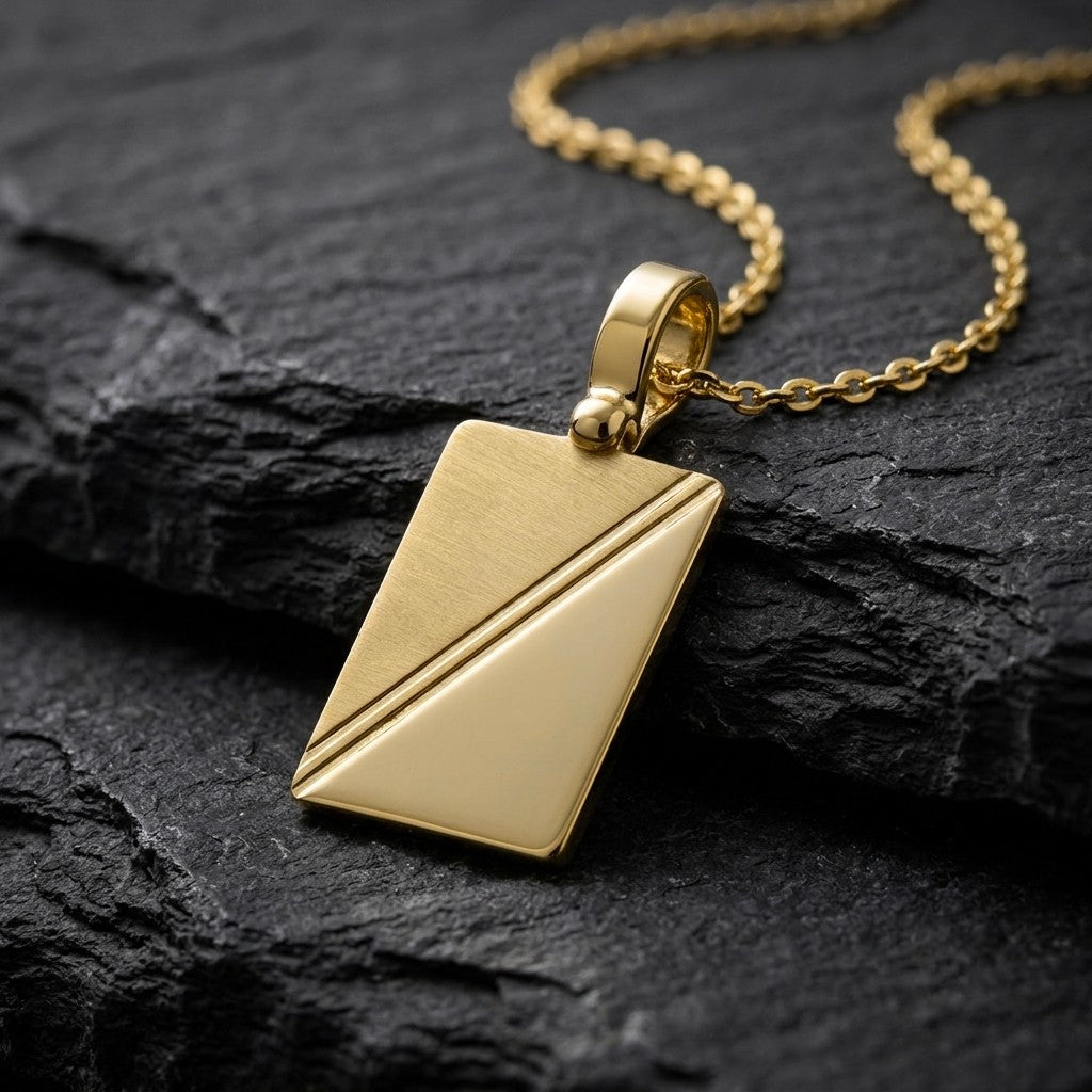 10K yellow gold rectangular tag pendant with diagonal satin and polished halves, 19 x 13 mm, 0.4 mm thick, on a yellow gold chain resting on dark slate stone
