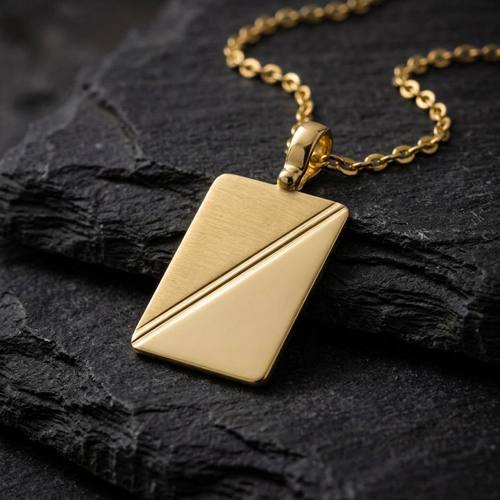 10K yellow gold rectangular tag pendant with diagonal satin and polished halves, 23 x 16 mm, 0.4 mm thick, on a yellow gold chain resting on dark slate stone