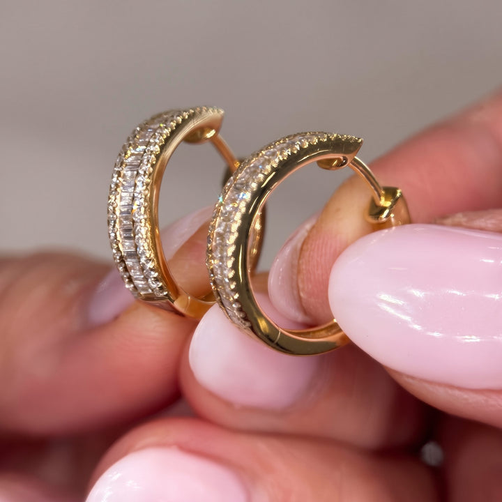 Hand holding RUDIX 14k yellow gold natural diamond baguette huggie hoop earrings showing diamond fire and scale