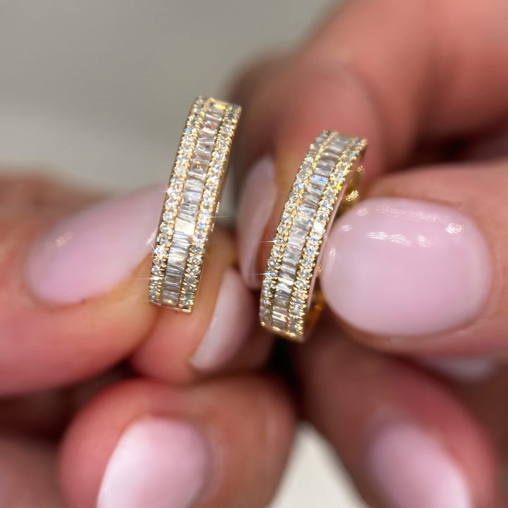 Macro hand shot of RUDIX 14k yellow gold natural diamond baguette huggie hoop earrings — triple-row baguette and round diamonds