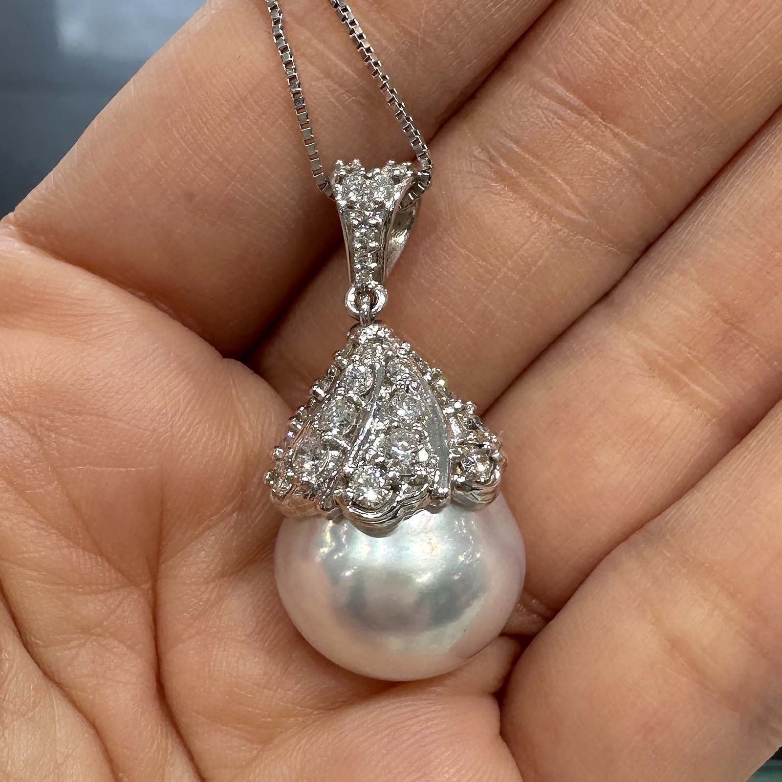 Hand holding a 16.6mm white South Sea pearl pendant in 18K white gold, adorned with small diamonds.