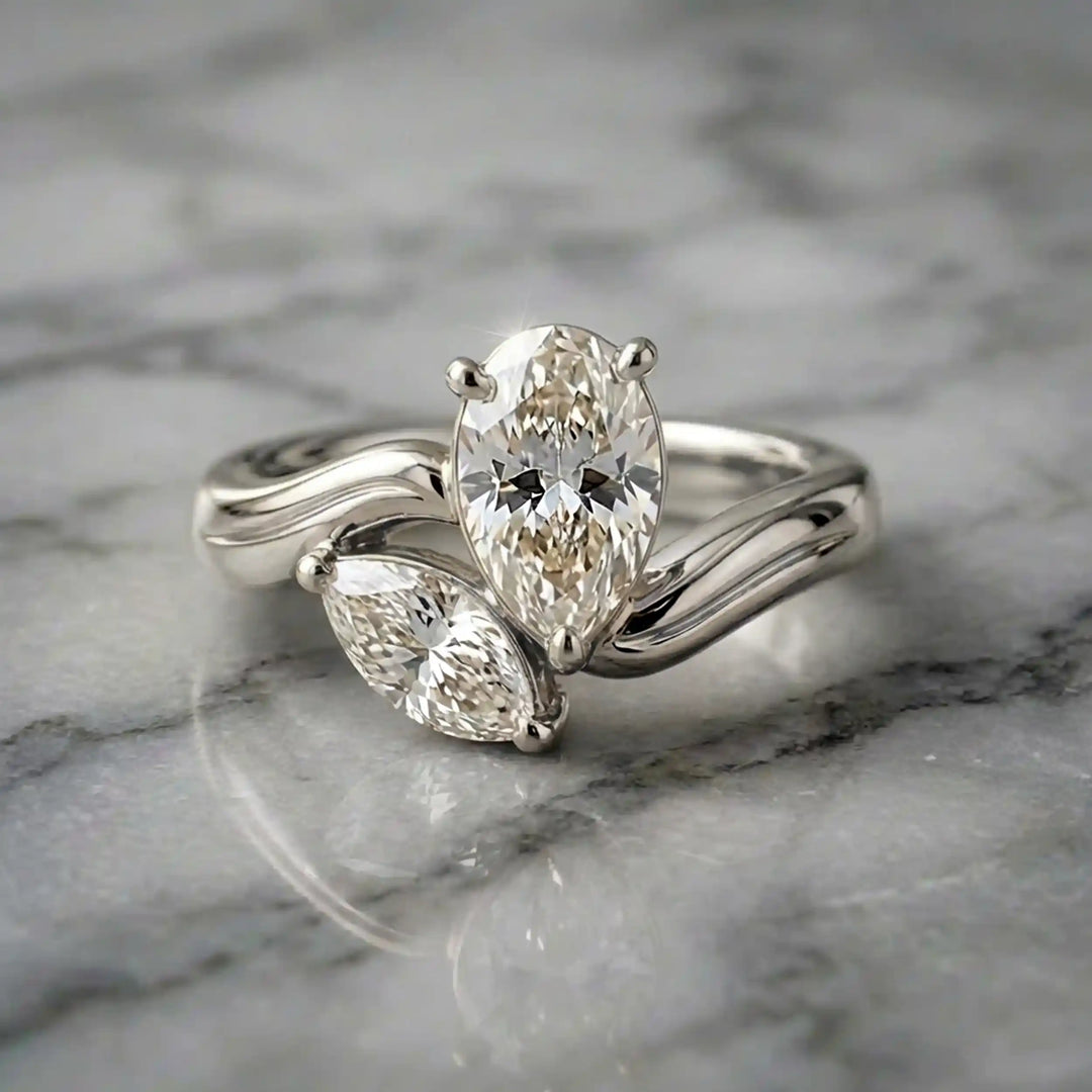 Lab-grown pear and marquise diamond toi et moi solitaire engagement ring displayed on marble surface.
