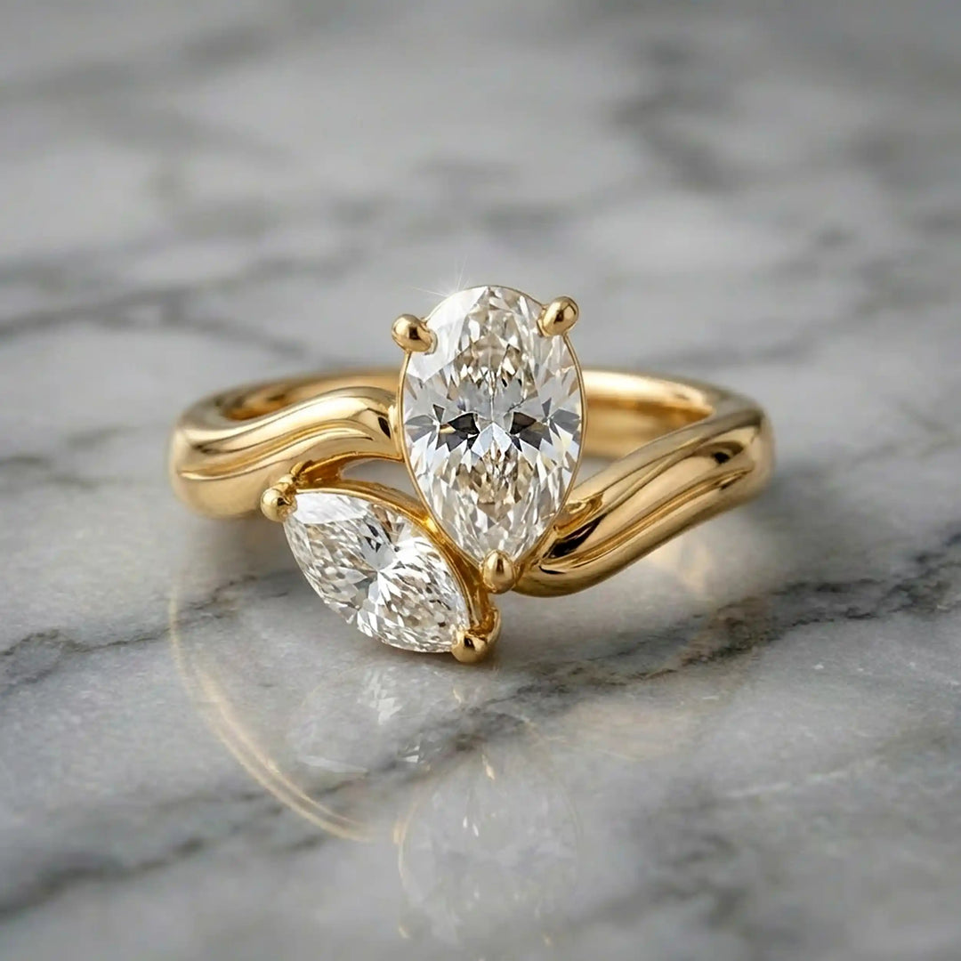 Lab-grown pear and marquise diamond toi et moi solitaire engagement ring displayed on marble surface.

