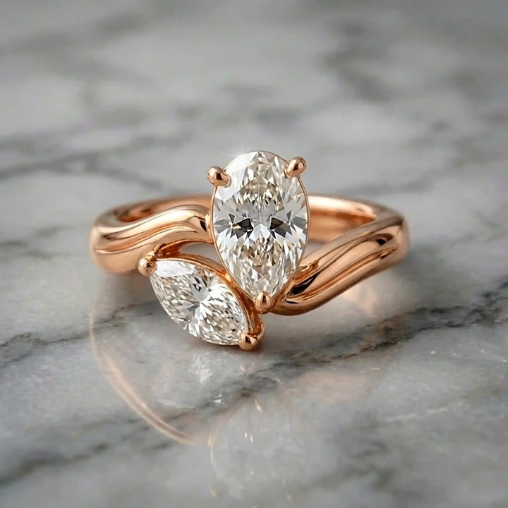 Lab-grown pear and marquise diamond toi et moi solitaire engagement ring displayed on marble surface.
