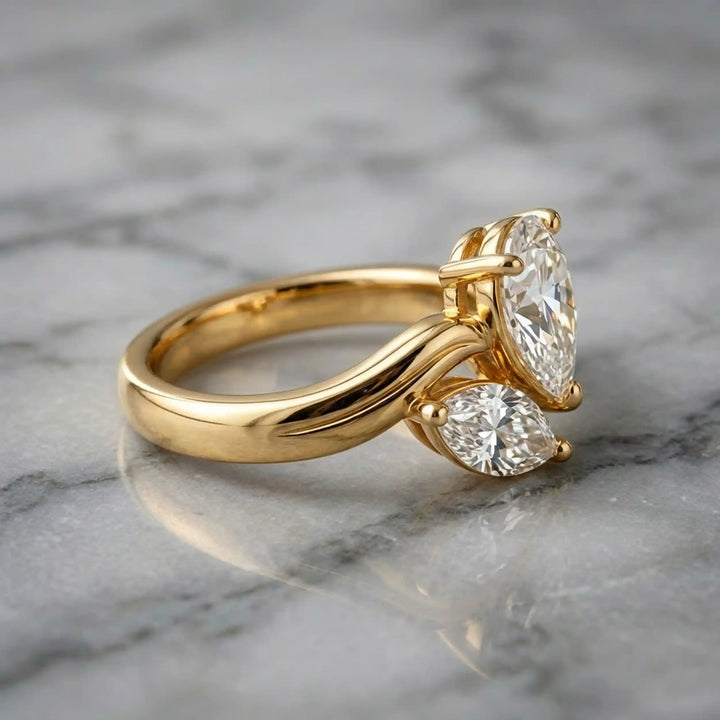 Lab-grown pear and marquise diamond toi et moi solitaire engagement ring displayed on marble surface.

