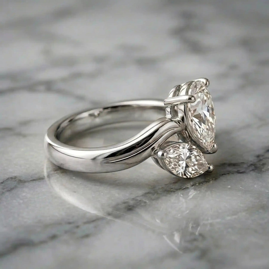 Lab-grown pear and marquise diamond toi et moi solitaire engagement ring displayed on marble surface.
