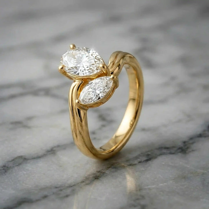 Lab-grown pear and marquise diamond toi et moi solitaire engagement ring displayed on marble surface.
