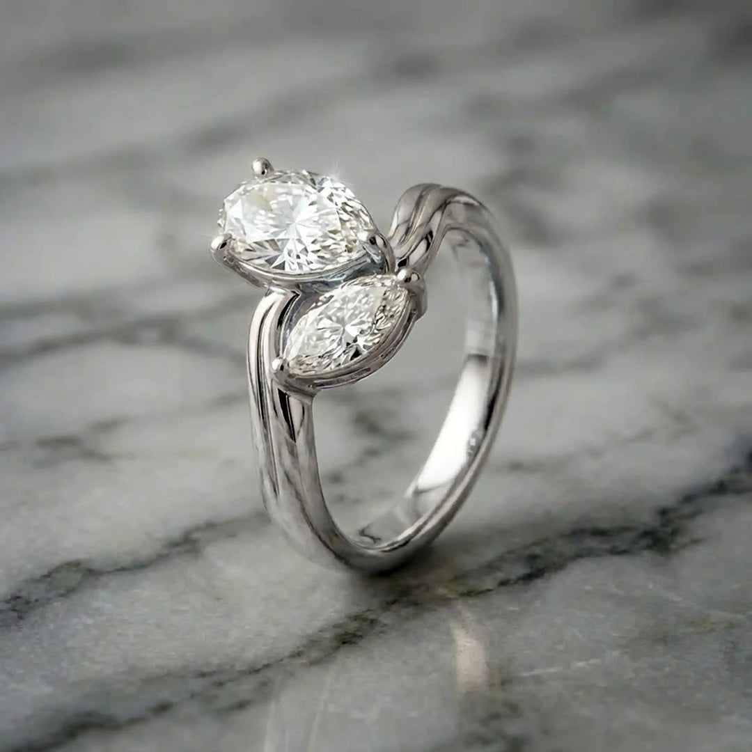 Lab-grown pear and marquise diamond toi et moi solitaire engagement ring displayed on marble surface.

