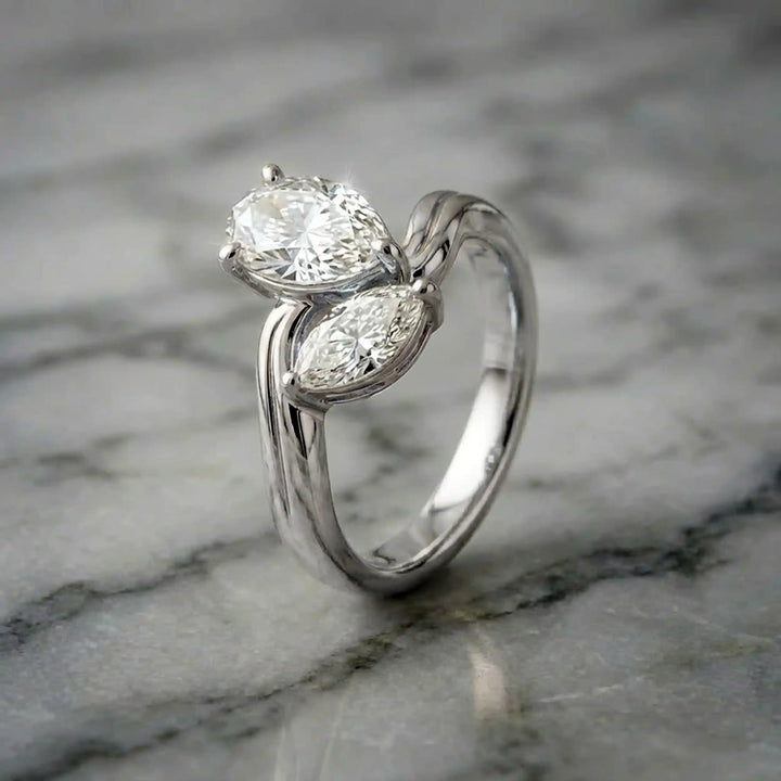 Lab-grown pear and marquise diamond toi et moi solitaire engagement ring displayed on marble surface.
