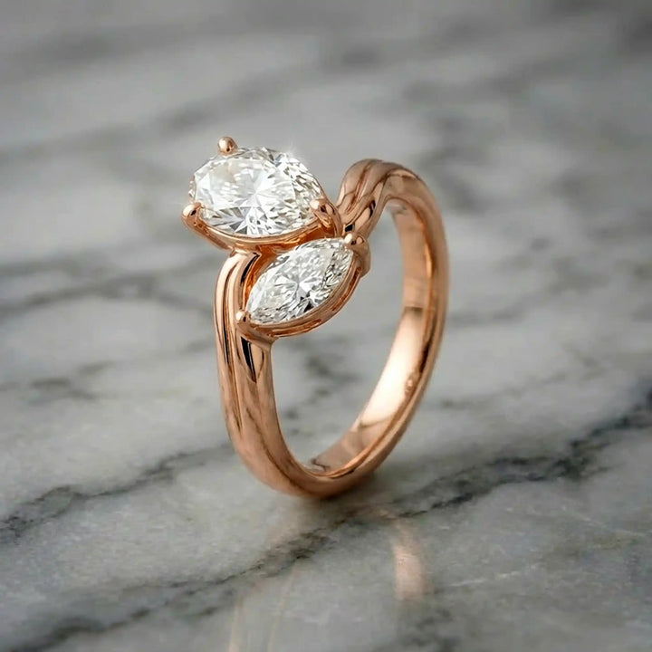 Lab-grown pear and marquise diamond toi et moi solitaire engagement ring displayed on marble surface.
