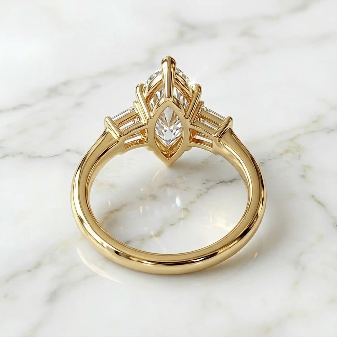 Three-stone marquise lab-grown diamond engagement ring displayed on marble surface.
