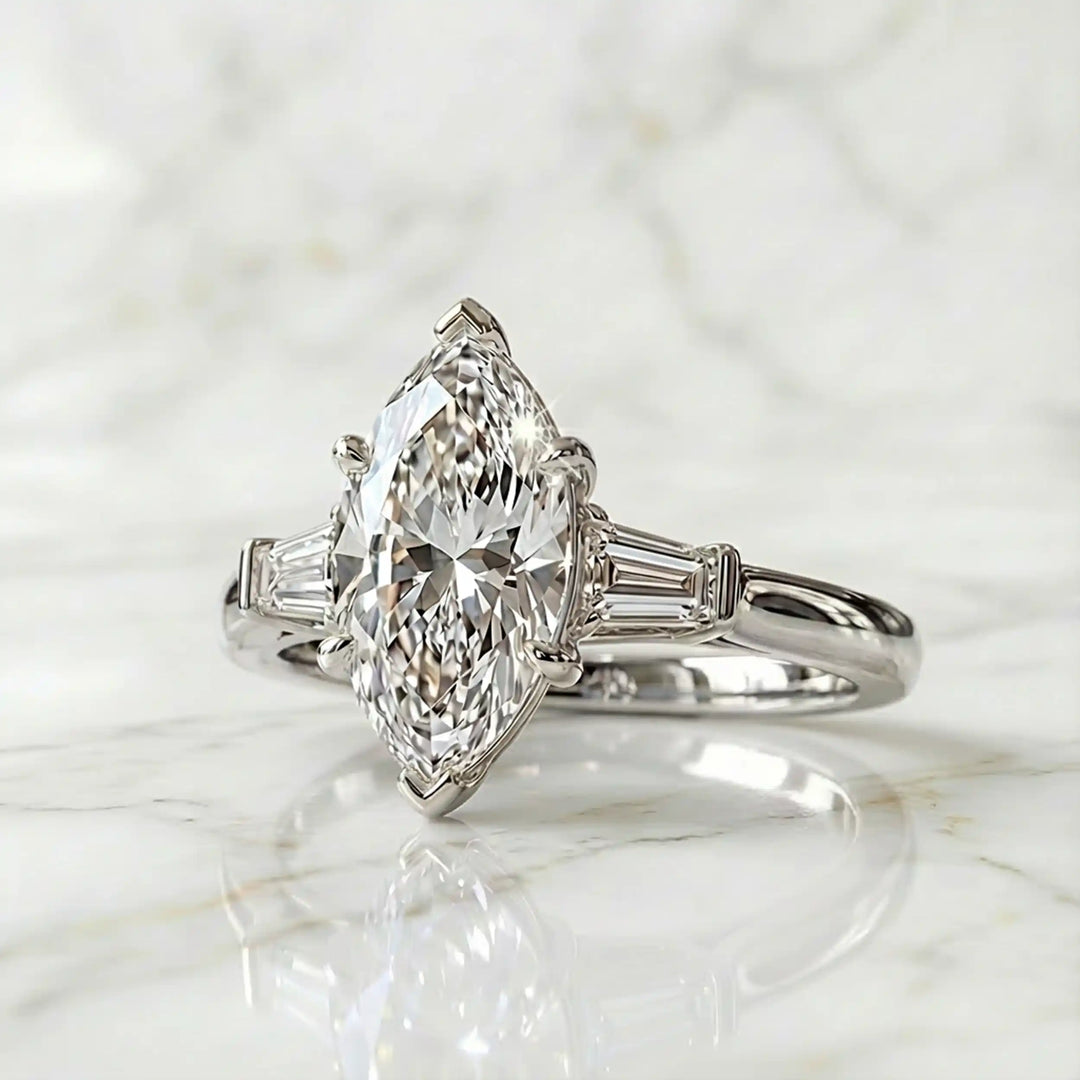 Three-stone marquise lab-grown diamond engagement ring displayed on marble surface.
