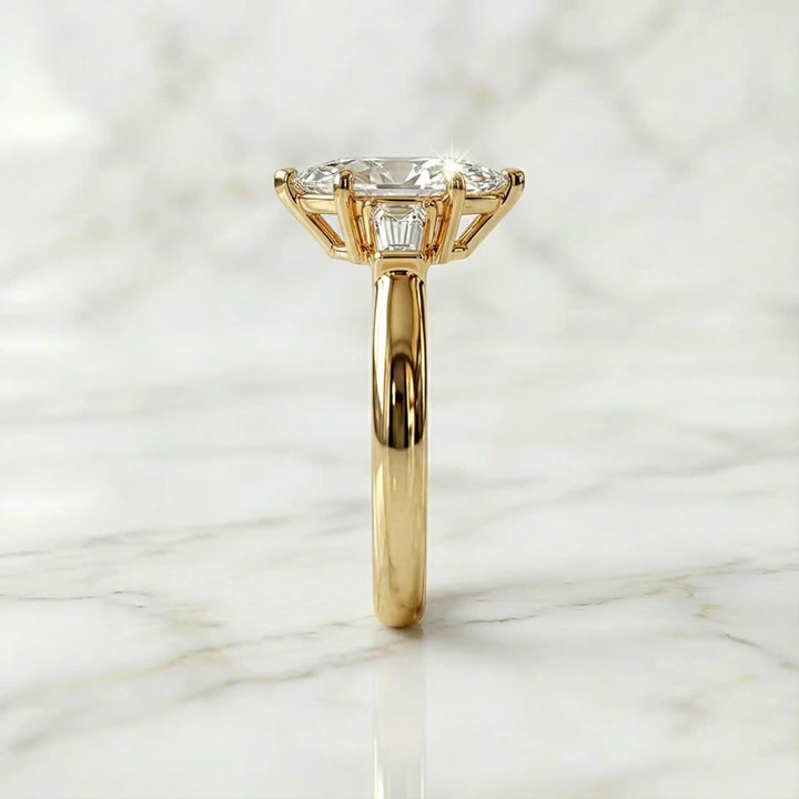 Three-stone marquise lab-grown diamond engagement ring displayed on marble surface.
