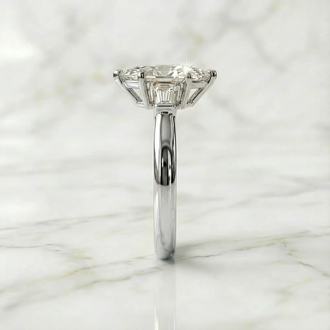 Three-stone marquise lab-grown diamond engagement ring displayed on marble surface.
