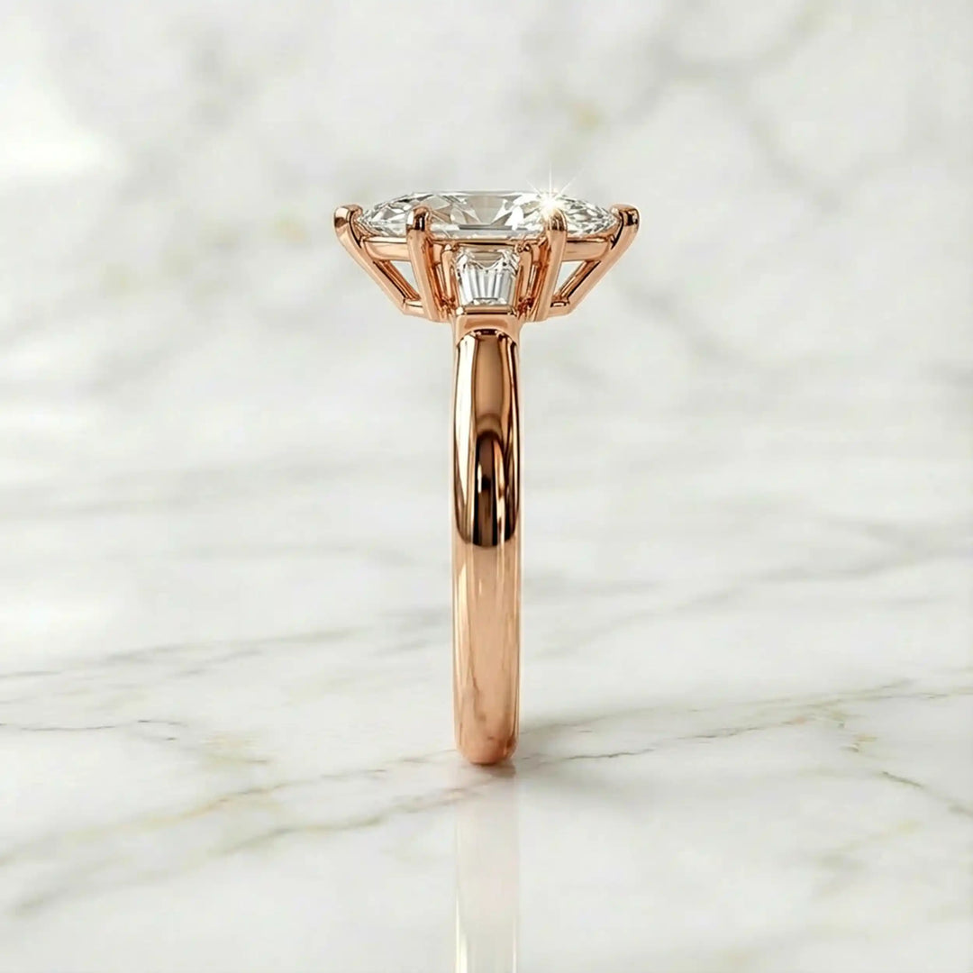 Three-stone marquise lab-grown diamond engagement ring displayed on marble surface.
