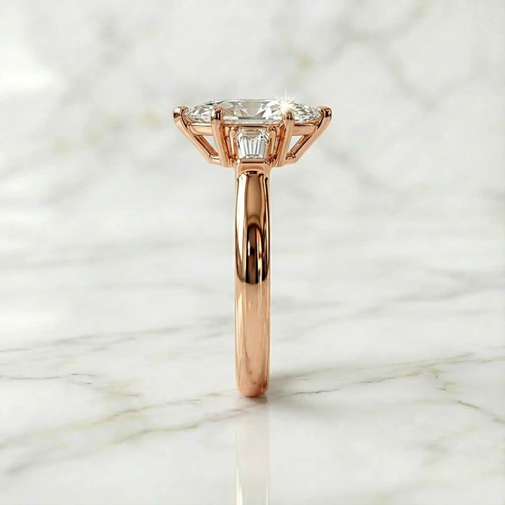 Three-stone marquise lab-grown diamond engagement ring displayed on marble surface.
