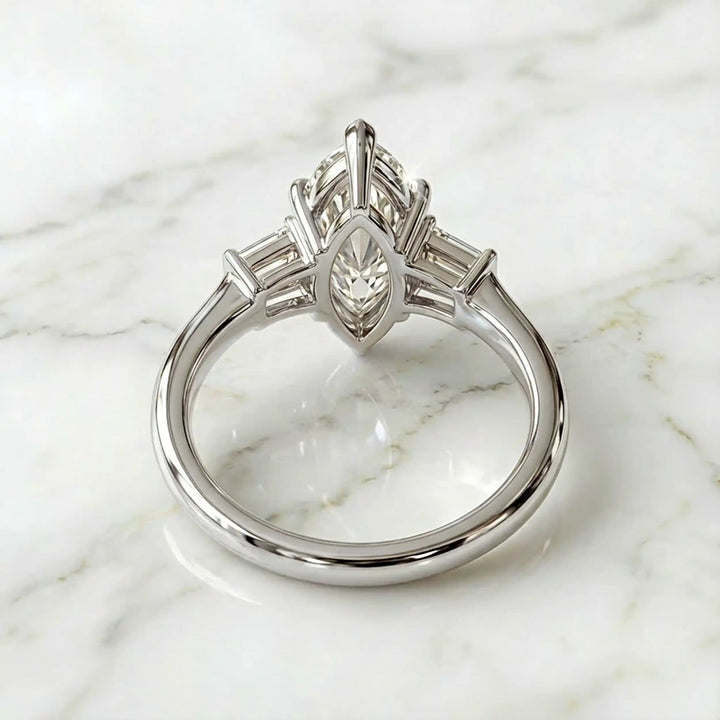 Three-stone marquise lab-grown diamond engagement ring displayed on marble surface.
