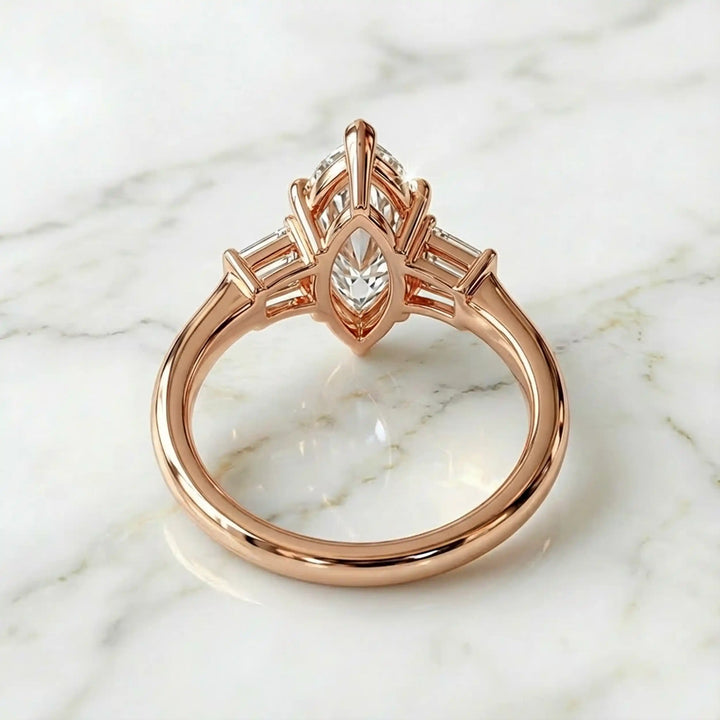 Three-stone marquise lab-grown diamond engagement ring displayed on marble surface.
