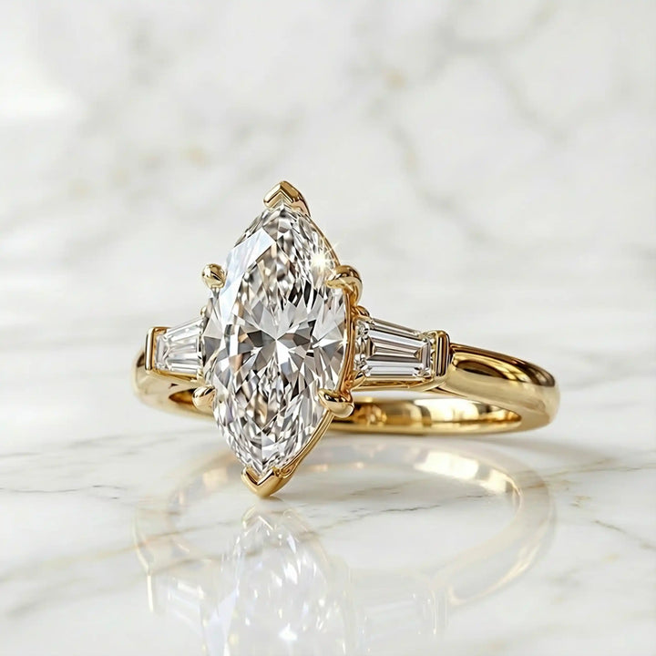 Three-stone marquise lab-grown diamond engagement ring displayed on marble surface.
