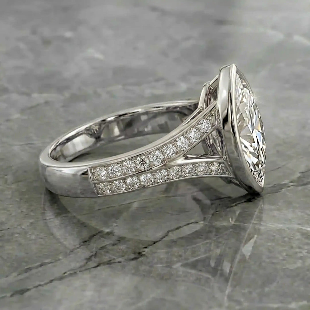 Marquise lab-grown diamond bezel engagement ring with split shank displayed on reflective surface.
