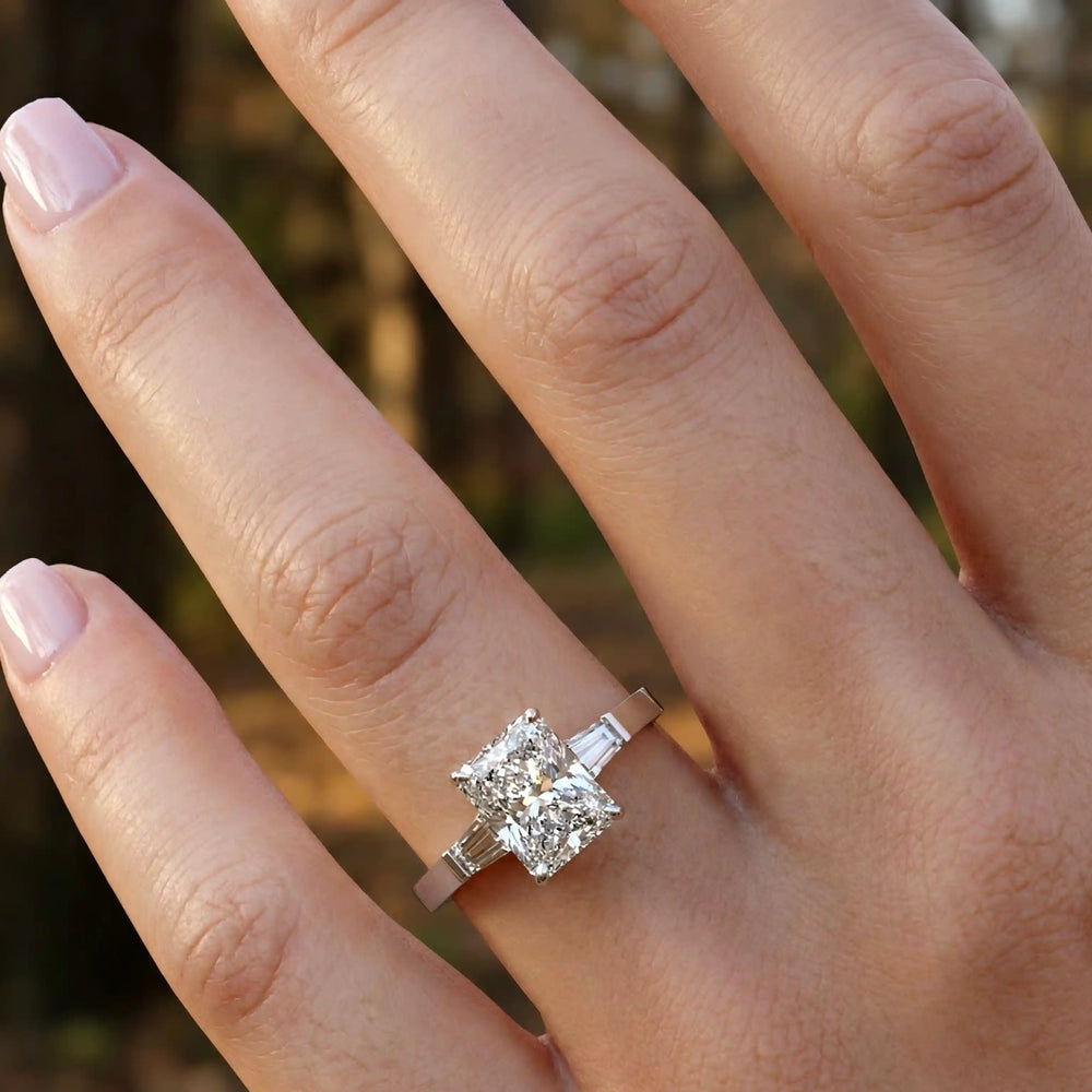 Radiant cut lab diamond three-stone engagement ring shown on hand.