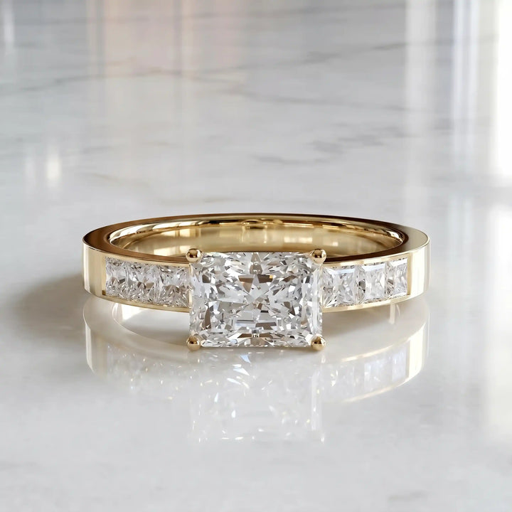 Radiant lab-grown diamond east-west engagement ring with channel-set princess side stones displayed on surface.